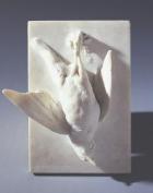 Marble sculpture of a dead songbird hanging upside down, pinned by its legs to a flat wall-like surface 