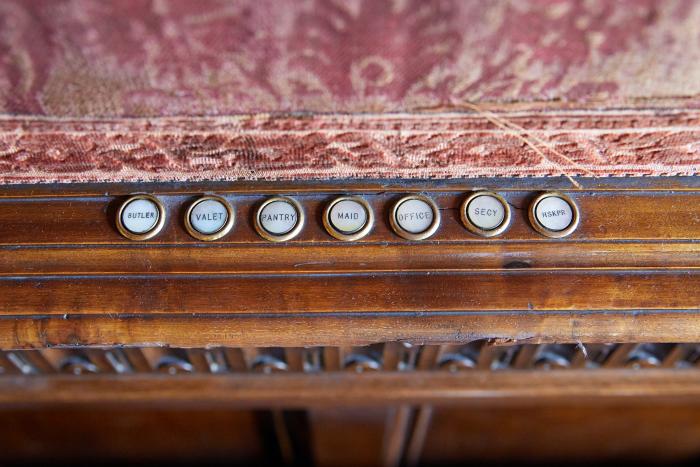 Seven white buttons on a wooden banister labeled Butler, Valet, Pantry, Maid, Office, Secretary, and Housekeeper