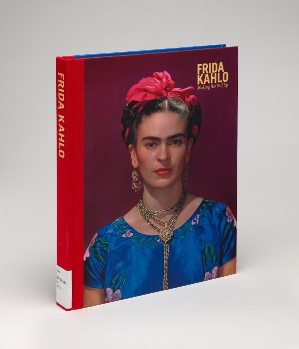 Cover against a gray background of "Frida Kahlo: Making Her Self Up," a purple and red cover featuring a close-up photo portrait of Kahlo