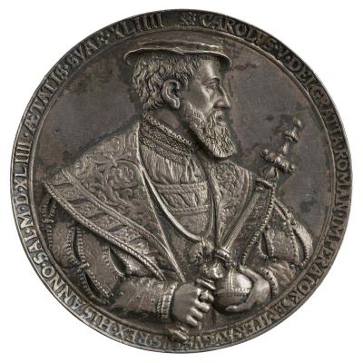 Silver medal of the emperor wearing a flat cap, pleated shirt and decorated cloak with the collar of the Order of the Golden Fleece. In his hands he olds the globe and the scepter
