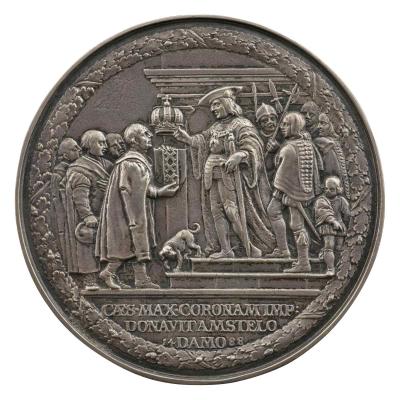 Silver medal of Emperor Maximillian I, in armor, holding gloves and resting on a sword, holds out the Imperial Crown to the magistrates of Amsterdam, holding the Arms of Amsterdam beneath the crown; between them, a dog slinking away from the emperor, behind whom are guards, courtiers, and a child.