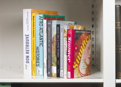 Vertical stack of ten colorful books on a white shelf