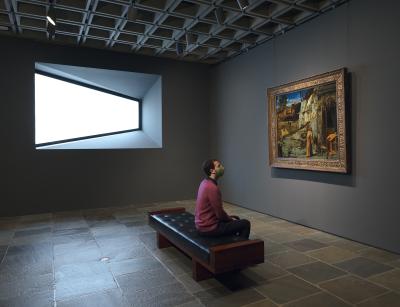 Man seated in a gallery between a trapezoidal window and Bellini's “St. Francis in the Desert”