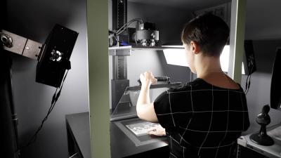 Library staff member scanning an archival photo at a workstation with lights and an overhead camera