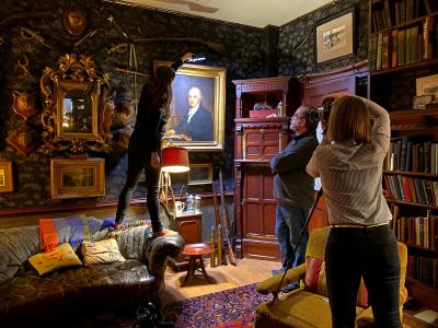 A photographer taking a photo of a portrait in a richly decorated room, with two others assisting.