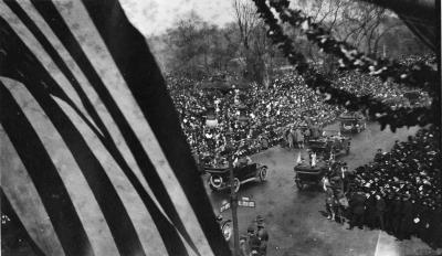 A military parade along Fifth Avenue, with an American flag and leafy garlands in the foreground