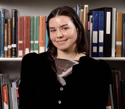 A woman with short brown hair smiling in front of shelves filled with books