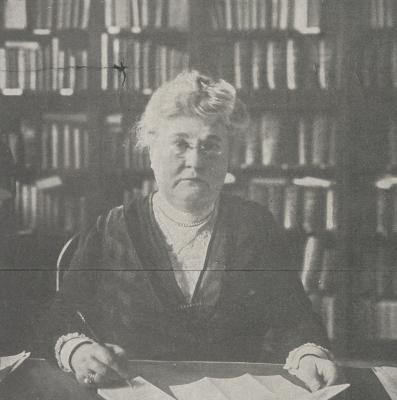 Detail from a newspaper clipping of a woman seated at a desk in front of large bookshelves