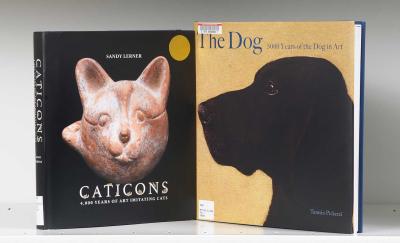 Two book covers on a shelf, one featuring a painting of a dog and the other a sculpture of a cat