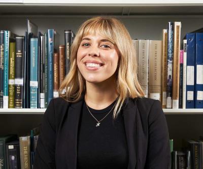 A blonde woman smiling in front of shelves filled with books