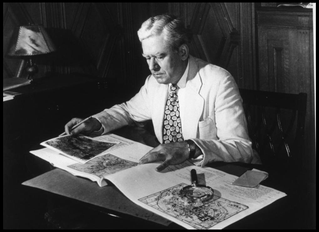 black and white photograph of william dinsmoor seated looking at maps and photographs